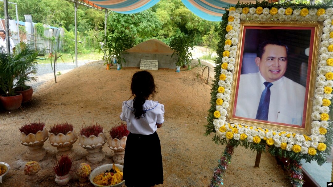 FILE - A girl stands by a portrait of Kem Ley, a Cambodian prominent political analyst, at his grave in Ang Takok, Cambodia, Nov. 20, 2016.