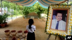 FILE - A girl stands by a portrait of Kem Ley, a Cambodian prominent political analyst, at his grave in Ang Takok, Cambodia, Nov. 20, 2016.