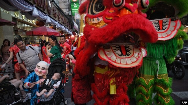 A laughing monk approaches a toddler as lion dancers perform on Yaowarat Road in Chinatown in Bangkok on Feb. 9, 2024, on the eve of the Lunar New Year.