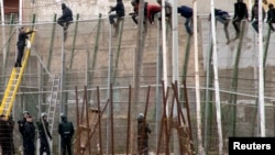 FILE - A Spanish Civil Guard officer (L) throws a sandwich to African migrants sitting at the top of a border fence during an attempt to cross into Spanish territories, between Morocco and Spain's north African enclave of Melilla, February 10, 2015. 