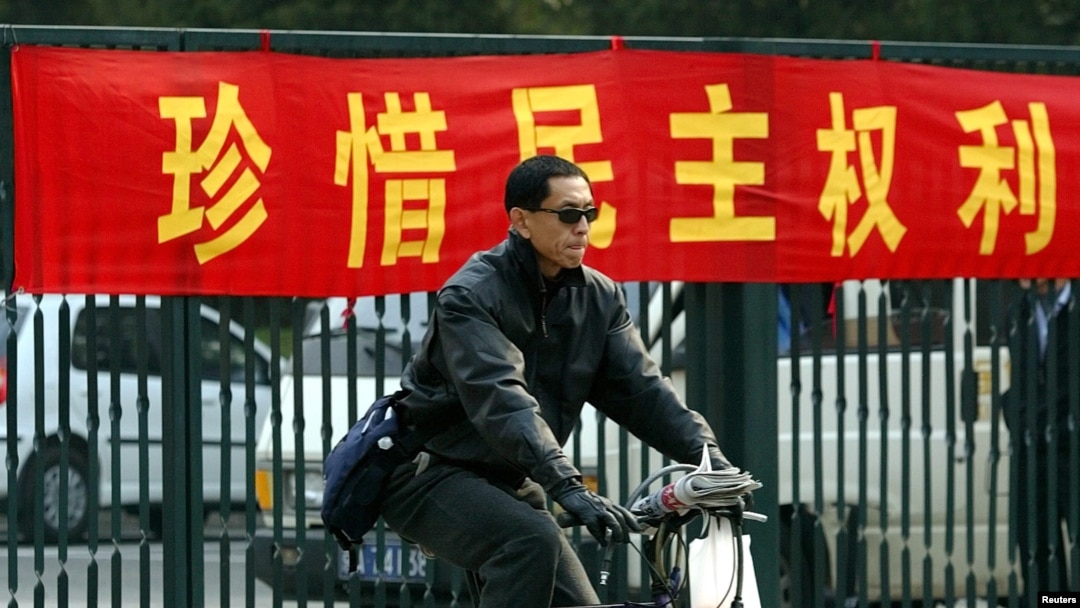 资料照：一名男子在北京街头骑车路过一条敦促市民”珍惜民主权利“的标语横幅。（2003年11月4日）