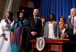 President Barack Obama signs the Violence Against Women Reauthorization Act of 2013 while Vice President Joe Biden looks on, in Washington, March 7, 2013.