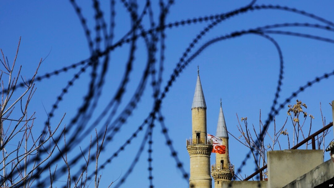 Bendera Turki dan Siprus Turki di kubah masjid Selimiye atau Agia Sofia, terlihat dari pagar kawat di wilayah penyangga PBB di Siprus (12/1).(AP/Petros Karadjias)