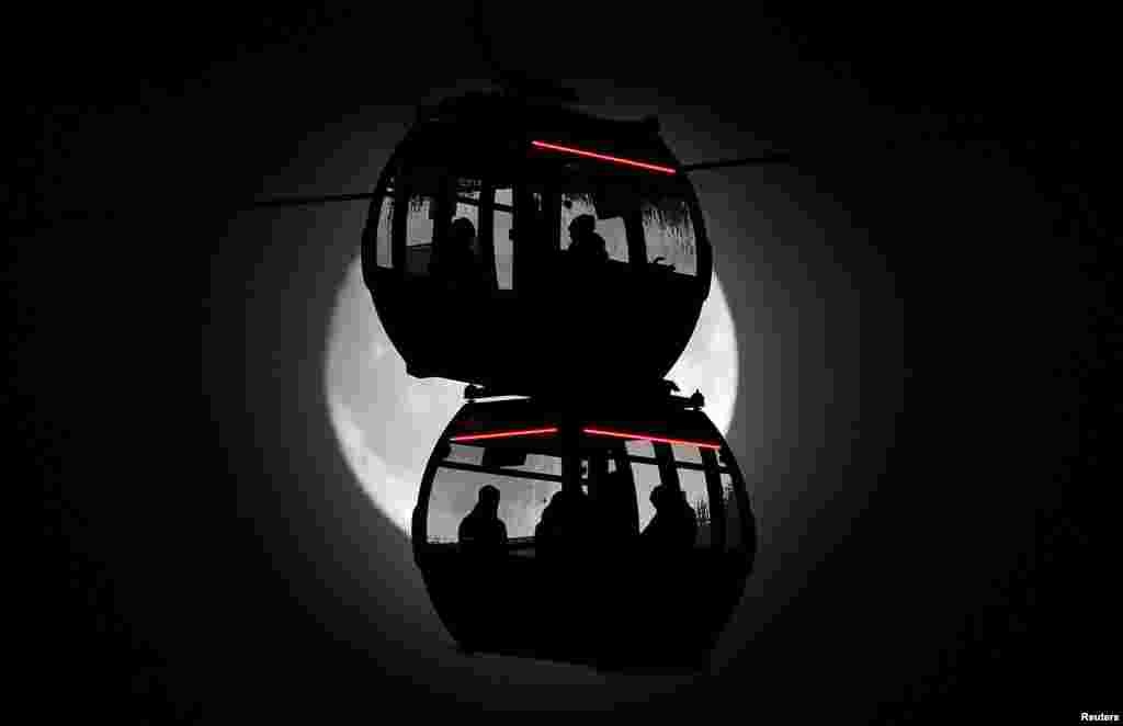 Passengers are seen silhouetted by the moon as they ride on the Emirates Airline cable car over the River Thames in London.