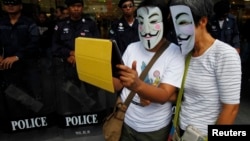 FILE - Anti-government protesters wearing Guy Fawkes masks use an iPad in front of riot policemen during a rally outside a shopping mall in Bangkok, June 9, 2013. 