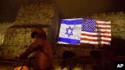 Un judío ortodoxo cruza en bicicleta un muro en el que se proyectan las banderas de Estados Unidos e Israel en la Ciudad Antigua de Jerusalén.