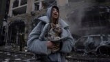 Ivanna warms her dog in front of a destroyed burning car after a recent Russian attack in Kyiv, Ukraine, Dec. 20, 2024.