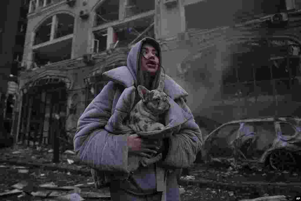 Ivanna warms her dog in front of a destroyed burning car after a recent Russian attack in Kyiv, Ukraine.