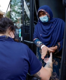 A woman takes the hand of a security officer as she and other people arrive at a processing center for refugees evacuated from Afghanistan at the Dulles Expo Center in Chantilly, Virginia, August 23, 2021.