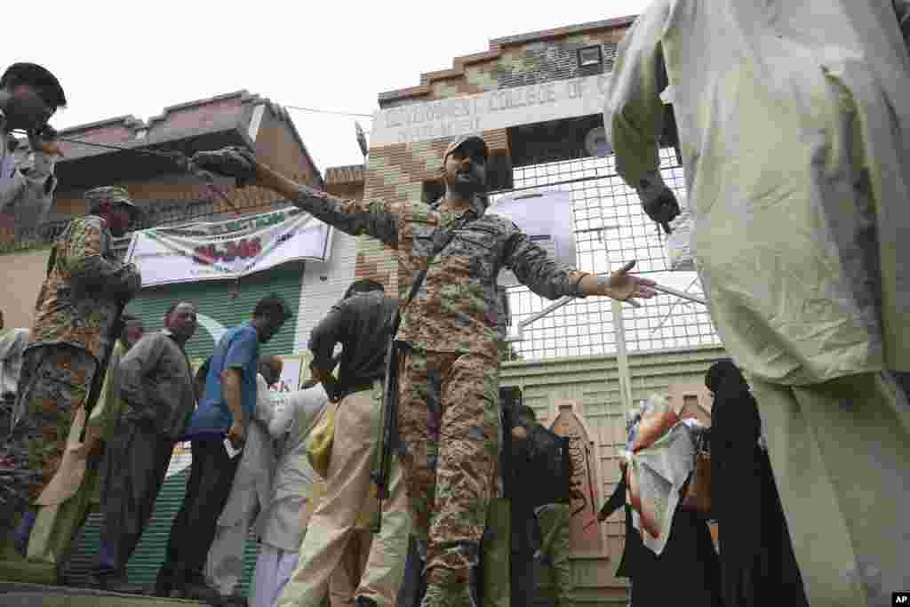 ایک فوجی اہلکار اس سینٹر کے باہر موجود انتخابی عملے کو ترتیب سے کھڑا ہونے کی ہدایت کر رہا ہے جہاں سے پولنگ کا سامان تقسیم کیا جارہا ہے۔