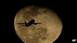 FILE - A passenger jet passes in front of a waning moon after taking off from Phoenix Sky Harbor International Airport, in Phoenix, Arizona, Feb. 11, 2020. Jill Marie Jones was arrested there last week before she could leave the country.