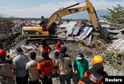 Rescue team members stand as heavy equipment clear debris to find bodies after an earthquake hit Petobo neighborhood in Palu, Indonesia, Oct. 5, 2018.