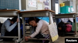 School children take shelter under desks during an earthquake simulation exercise in an annual evacuation drill at an elementary school in Tokyo, March 10, 2017.