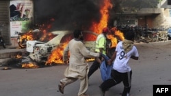 Pakistani volunteers and local residents carry the dead body of a protester beside a burning car after gunmen opened fire on a rally in Karachi, May 22, 2012.