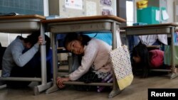 FILE - School children take shelter under desks during an earthquake simulation exercise in an annual evacuation drill at an elementary school in Tokyo, March 10, 2017.