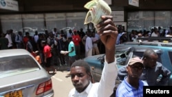 FILE - A man holds old notes in front of people queueing for cash at a local bank during a demonstration against the new ‘bond notes’ that came into circulation this week in an attempt to ease chronic cash shortages, in the capital Harare, Zimbabwe, Nov. 30, 2016.