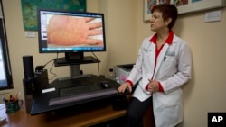 FILE - University of Miami dermatologist Dr. Anne Burdick checks the computer screen in her Miami office as she discusses telemedicine, April 8, 2014.
