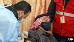 FILE - A mask-clad Jordan-based Syrian refugee receives a COVID-19 vaccination at a governmental medical center in Mafraq in northern Jordan, Jan. 18, 2021. 