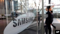 FILE - An employee walks past the Samsung Electronics Co. logo at its office in Seoul, Jan. 31, 2018. This month, two former Samsung employees were sentenced to two years in prison for trying to leak Samsung’s OLED secrets to China.