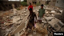 People walk on the wreckage of a house destroyed by an air strike last year that was targeting al Qaeda-linked militants, in the southern Yemeni town of Jaar, February 1, 2013.