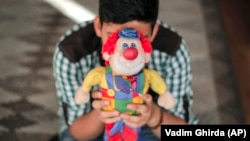 A boy living in a family-style home for abandoned children poses for a photo covering his face with a clown doll in Bucharest, Romania, on Wednesday, Nov. 1, 2017. (AP Photo/Vadim Ghirda)