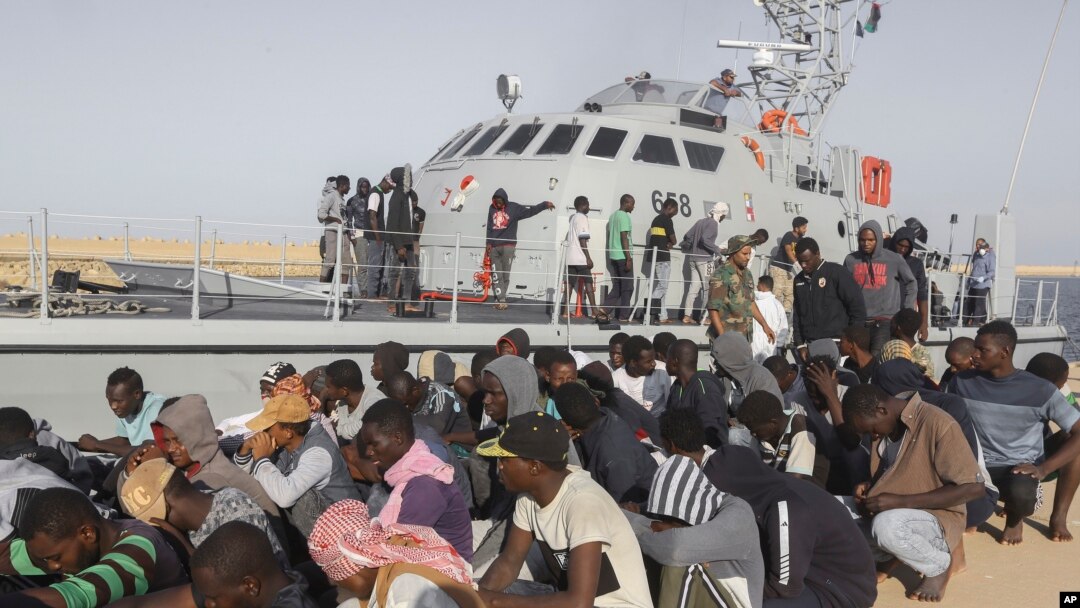 Rescued migrants are seated next to a coast guard boat in the city of Khoms, around 120 kilometers (75 miles) east of Tripoli, Libya, Oct. 1, 2019. 