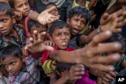 FILE - Rohingya Muslim children, who crossed over from Myanmar into Bangladesh, stretch out their arms out to collect chocolates and milk distributed by Bangladeshi men at Taiy Khali refugee camp, Bangladesh, Sept. 21, 2017.