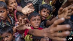 FILE - Rohingya Muslim children, who crossed over from Myanmar into Bangladesh, stretch out their arms out to collect chocolates and milk distributed by Bangladeshi men at Taiy Khali refugee camp, Bangladesh, Sept. 21, 2017. 