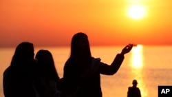 FILE— A parishioner is silhouetted against the rising sun as she prays during an Easter sunrise service held by Park Community Church Sunday, April 4, 2021, at North Avenue Beach in Chicago. On Easter morning, many Christians wake before dawn. 