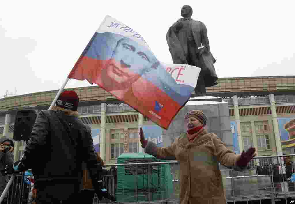 A woman dances in front of a monument of Soviet State founder Vladimir Lenin, after a rally to support presidential candidate and Russia's current Prime Minister Vladimir Putin, outside the Luzhniki stadium on the Defender of the Fatherland Day in Moscow,