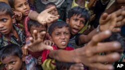 FILE - Rohingya Muslim children, who crossed over from Myanmar into Bangladesh, stretch out their arms out to collect chocolates and milk distributed by Bangladeshi men at Taiy Khali refugee camp, Bangladesh, Sept. 21, 2017. 