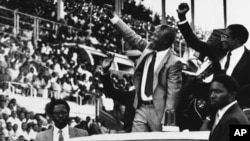 Nelson Mandela, l'ancien président d'Afrique du Sud, au centre, et Robert Mugabe, l'ancien président du Zimbabwe, à droite, saluent la foule pour Mandela Day à Harare, au Zimbabwe, le 5 mars 1990.