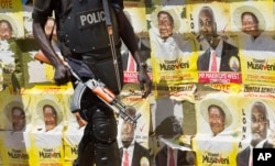 FILE - An armed Ugandan riot policeman patrols past campaign posters for long-time President Yoweri Museveni, as well as local members of Parliament, on a street in Kampala, Uganda, Feb. 17, 2016.