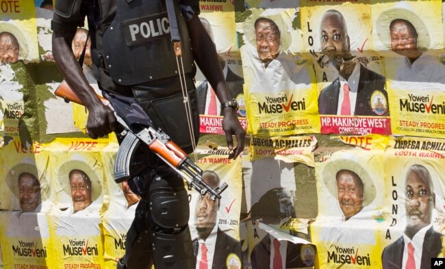 FILE - An armed Ugandan riot policeman patrols past campaign posters for long-time President Yoweri Museveni, as well as local members of Parliament, on a street in Kampala, Uganda, Feb. 17, 2016.