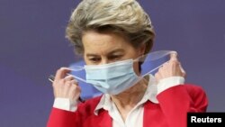 European Commission President Ursula Von Der Leyen removes her protective face mask as she arrives for a news conference on vaccine strategy in Brussels, Belgium, January 8, 2021