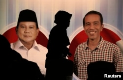 FILE - A woman walks past a poster of Indonesia's presidential candidates Prabowo Subianto (L) and Joko Widodo during a debate in Jakarta June 15, 2014.