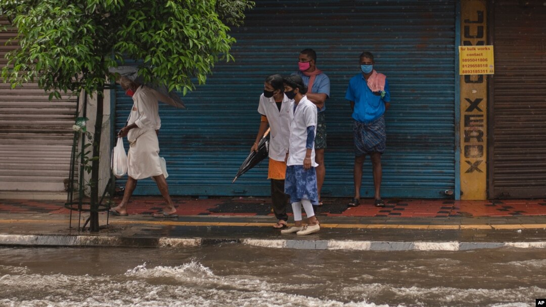 Two medical workers wearing masks as a precaution against the coronavirus assess the water level as they try to cross a flooded street during heavy rainfall in Kochi, Kerala state, India, Aug. 7, 2020.