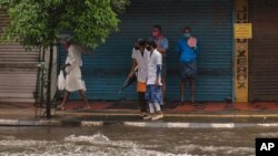 Two medical workers wearing masks as a precaution against the coronavirus assess the water level as they try to cross a flooded street during heavy rainfall in Kochi, Kerala state, India, Aug. 7, 2020.