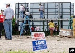 FILE - A sign against the Keystone XL pipeline is planted in the foreground, as workers and volunteers assemble solar panels in a corn field belonging to Jim Carlson, directly in the path of the proposed pipeline, in Silver Creek, Nebraska, July 29, 2017.