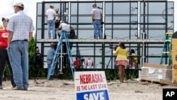 A sign against the Keystone XL pipeline is planted in the foreground, as workers and volunteers assemble solar panels in a corn field belonging to Jim Carlson, directly in the path of the proposed pipeline, in Silver Creek, Nebraska, July 29, 2017.