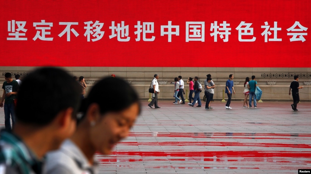 资料照：人们走过北京天安门广场竖立的一幅宣传中国特色社会主义道路的巨幅标语。（2012年6月3日）