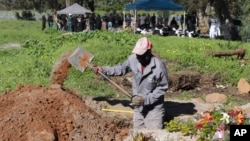 Un fossoyeur travaille dans la section COVID-19 du cimetière de Maitland au Cap, en Afrique du Sud, le 15 juillet 2020 alors qu'un enterrement a lieu en arrière-plan. 