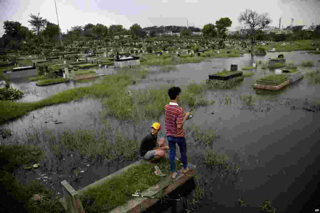 Dua orang remaja berdiri di atas makam sambil memancing ikan saat banjir menggenangi sebuah komplek pemakaman di Jakarta.