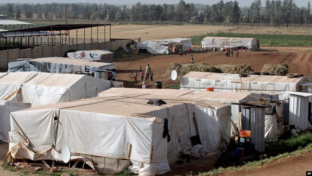 Syrian refugees walk outside their tents at a Syrian refugee camp in the eastern Lebanese town of Majdal Anjar, Lebanon, June 19, 2014.