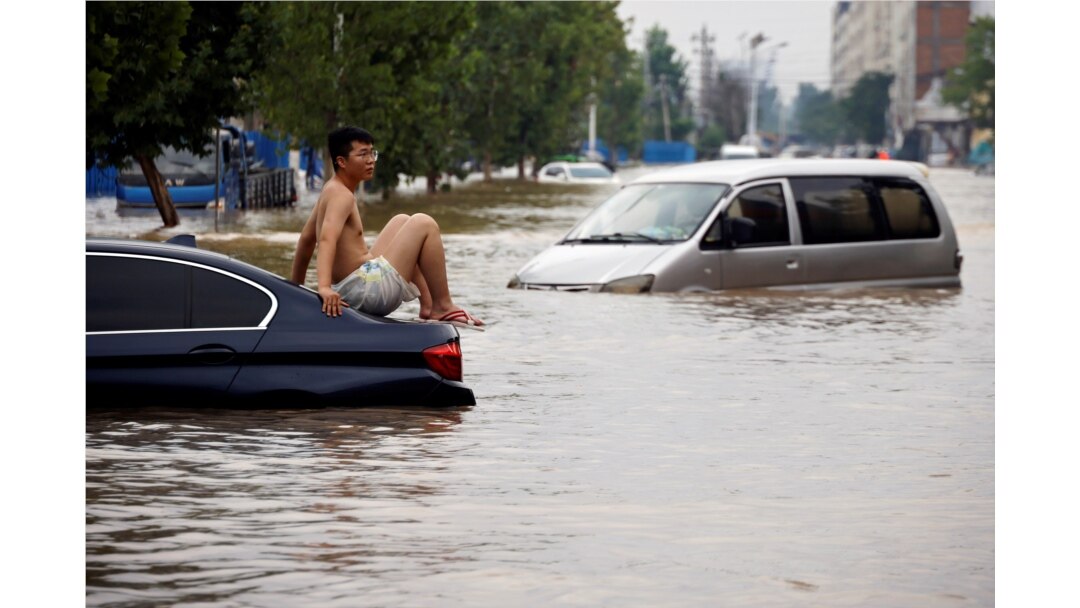 FILE - A man sits on a stranded vehicle on a flooded road following heavy rainfall in Zhengzhou, Henan province, China, July 22, 2021.