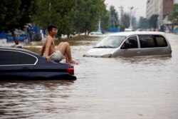 FILE - A man sits on a stranded vehicle on a flooded road following heavy rainfall in Zhengzhou, Henan province, China, July 22, 2021.