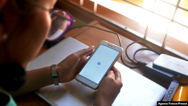 FILE - A woman uses her mobile phone to check Facebook in Naypyidaw, March 16, 2021, as Myanmar authorities ordered telecommunications companies to restrict their services on the mobile data networks, following the Feb. 1 military coup.