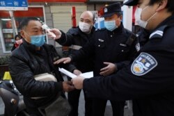 A community worker measures the body temperature of a man as police officers inspect his documents at a checkpoint set up at an entrance to a street in Wuhan, Hubei province, China, Feb. 20, 2020.