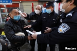 A community worker measures the body temperature of a man as police officers inspect his documents at a checkpoint set up at an entrance to a street in Wuhan, Hubei province, China, Feb. 20, 2020.