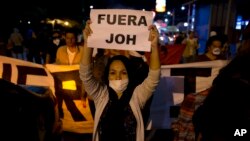 A woman holds a sign with a message that reads in Spanish "Get out JOH" during a protest against Honduran President Juan Orlando Hernandez, in Tegucigalpa, Honduras, Jan. 26, 2018. Hernandez was awarded the electoral win last month despite the disputed vote tally.
